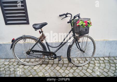 Vintage-Fahrrad mit einem bezaubernden Korb mit Blumen, der an eine rustikale Mauer in der Stadt lehnt Stockfoto