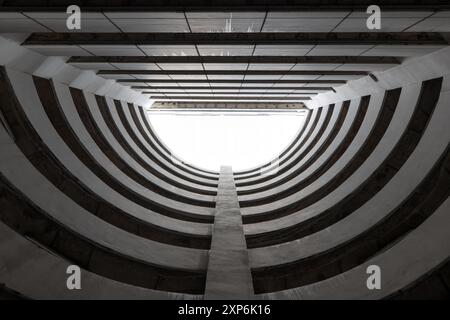 Blick von unten auf die runde Parkgarage vor weißen Wolken und blauem Himmel. Automatisches Kreisparksystem. Abstraktes Architekturgebäude. Stockfoto