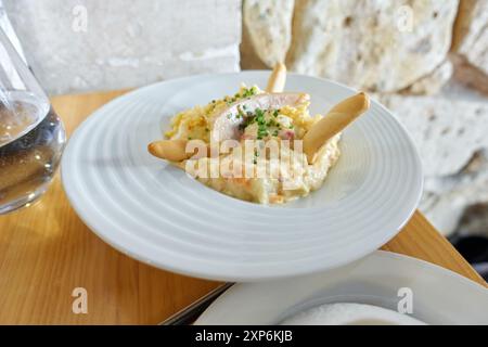 Typisch spanische Tapa, russischer Salat, mit gekochten Kartoffeln und Ei, Karottenstücken, Erbsen, Mayonnaise, Thunfischbauch, geschnittener Schnittlauch und Brotstäbchen Stockfoto