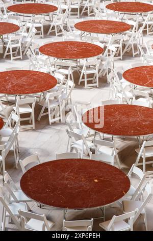 Reihen von runden Tischen und Stühlen stehen in einem hellen Saal, die auf Gäste warten. Stockfoto