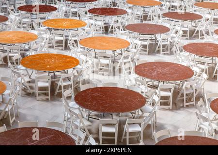 Reihen von runden Tischen und Stühlen stehen in einem hellen Saal, die auf Gäste warten. Stockfoto