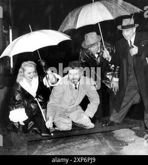 JAMES MASON legte 1954 seine Hand und Fußabdrücke in Zement im Grauman's Chinese Theatre in Hollywood ab, während seine Co-Stars JANET LEIGH und VICTOR McLAGLEN und Fox Movie Executive CHARLES P. SKOURAS ihn vor dem strömenden Regen schützen, als sie PRINCE VALIANT drehten regisseur HENRY HATHAWAY Twentieth Century Fox Stockfoto