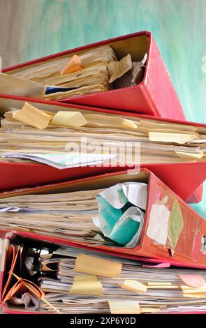 Unordentliche Aktenordner und Geschäftsunterlagen, Bürokratie, überarbeitet, übertroffen, übertroffen, das Uhrengeschäftskonzept auf unordentlichem blauem Hintergrund. Stockfoto