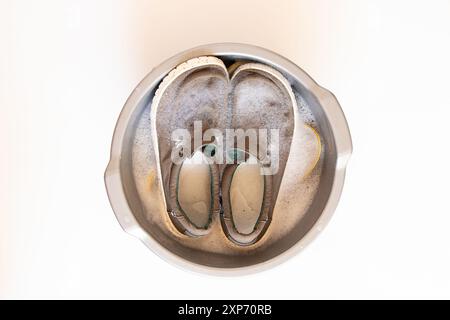 Helle Herrenschuhe werden in einer Schüssel mit Wasser auf weißem Hintergrund gewaschen, Schuhe in einer Schüssel waschen Stockfoto