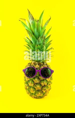 Ananas mit violetter Sonnenbrille auf gelbem Hintergrund Stockfoto
