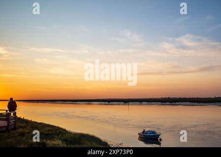 St-Valery-sur-Somme, Frankreich: Sonnenuntergang über der Flussmündung des Flusses Somme mit einem einzigen Mann, der vor einem orange-blauen Himmel steht. Stockfoto