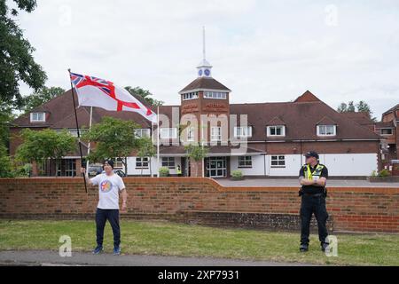 Ein einsamer Demonstrant, der von einem Polizisten während einer Demonstration vor dem Potters International Hotel in Aldershot, Hampshire beobachtet wurde, nach den Messerstechangriffen am Montag in Southport, bei denen drei kleine Kinder getötet wurden. Bilddatum: Sonntag, 4. August 2024. Stockfoto