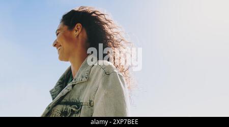 Glückliche, sorglose Frau lächelt und genießt einen fröhlichen Tag im Freien mit dem blauen Himmel im Hintergrund. Seitenprofil einer glücklichen Frau, die in der Sonne lächelt Stockfoto