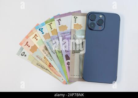 Syrische Geldscheine mit Smartphone auf weißem Hintergrund. Mobiles Banking. Stockfoto