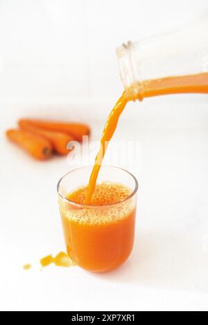 Frischer Karottensaft wird in ein klares Glas gegossen und zeigt die leuchtende orange Farbe und Frische des Safts. Stockfoto