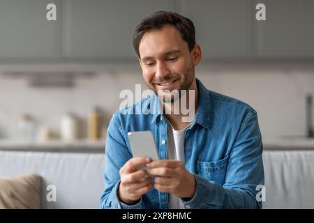 Mann lächelt, während er ein Smartphone auf der Couch benutzt Stockfoto