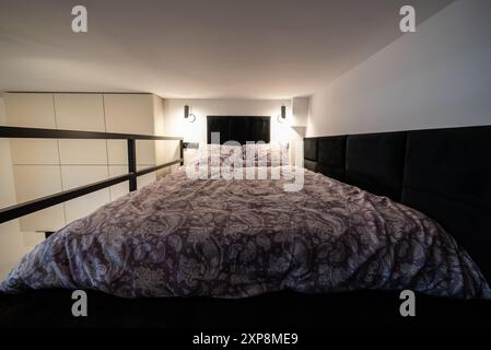 Modernes Studio-Apartment mit einem Schlafzimmer im Zwischengeschoss. Das Innere eines Hotelschlafzimmers mit Bett und Kissen. Kleines und modernes Apartment mit Zwischengeschoss Stockfoto