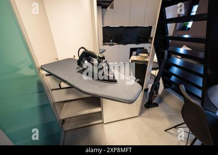 Kleines und modernes Studio-Apartment mit Zwischengeschoss-Schlafzimmer. Bügeleisen auf dem Bügeltisch. Bügelmaschine in einem modernen Zuhause. Bügelkleidung. Stockfoto