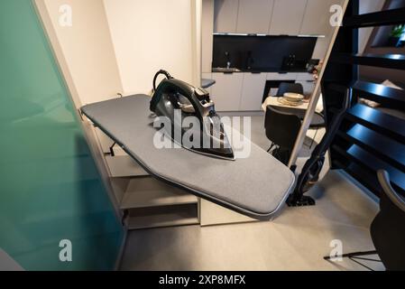 Kleines und modernes Studio-Apartment mit Zwischengeschoss-Schlafzimmer. Bügeleisen auf dem Bügeltisch. Bügelmaschine in einem modernen Zuhause. Bügelkleidung. Stockfoto