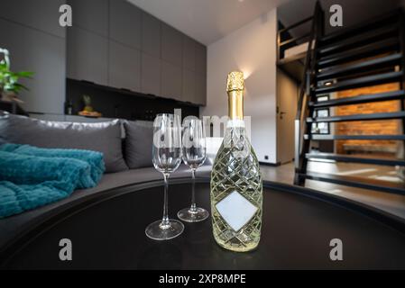 Moderne Küche, die mit dem Wohnzimmer verbunden ist, in einem kleinen, modernen Apartment. Sektflasche und Gläser auf schwarzem Tisch im modernen Wohnzimmer. Moderner Pelz Stockfoto