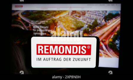 Person mit Mobiltelefon mit Logo des deutschen Entsorgungsunternehmens Remondis SE Co. KG vor der Business-Webseite. Schwerpunkt auf dem Display des Telefons. Stockfoto