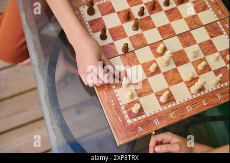 Draufsicht auf zwei Personen, die an einem Schachspiel auf einem Glastisch teilgenommen haben, mit Schwerpunkt auf Strategie und Konzentration. Ideal für Brettspiele, Strateg Stockfoto