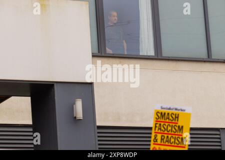 Rotherham, Großbritannien. AUGUST 2024. Die im Hotel untergebrachten Personen blicken aus den Fenstern auf die Menschenmenge, während Hunderte von Polizisten und Demonstranten vor einem Holiday Inn Express am Manvers Way, Rotherham, aufeinander treffen. Die Demonstranten des rechten Flügels, die von Sir Kier Starmer als „Gangster“ beschrieben wurden, zündeten Eigentum an, zerschlugen Glas und kämpften mehrere Stunden mit der Polizei. Mehrere Verhaftungen und Verletzungen von Aufständischen und Polizei. Credit Milo Chandler/Alamy Live News Stockfoto