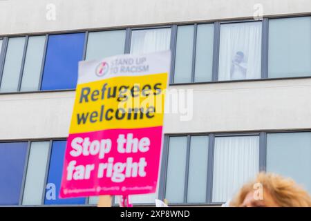 Rotherham, Großbritannien. AUGUST 2024. Migranten, die im Hotel untergebracht sind, blicken aus den Fenstern auf die Menschenmenge, während Hunderte von Polizisten und Demonstranten vor einem Holiday Inn Express am Manvers Way, Rotherham, aufeinander treffen. Die Demonstranten des rechten Flügels, die von Sir Kier Starmer als „Gangster“ beschrieben wurden, zündeten Eigentum an, zerschlugen Glas und kämpften mehrere Stunden mit der Polizei. Mehrere Verhaftungen und Verletzungen von Aufständischen und Polizei. Credit Milo Chandler/Alamy Live News Stockfoto