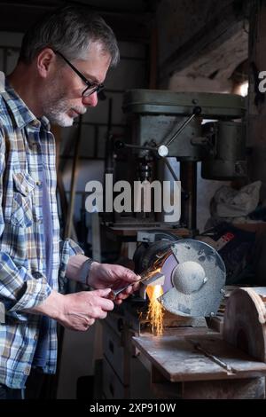 DIY-Mann, der einen Meißel in einer Werkstatt schärft Stockfoto