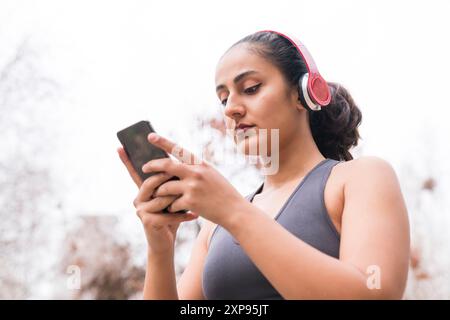 Junge Frau überprüft Fitness-Tracker nach dem Training. Fitnesskonzept mit Kopfhörer und Smartphone. Stockfoto