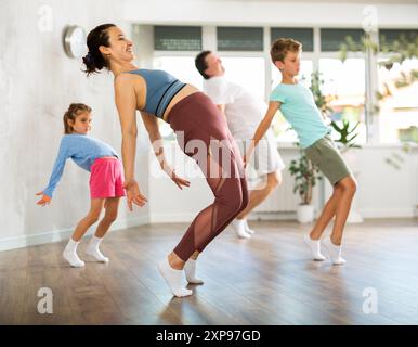 Glückliche Frau mittleren Alters, die mit ihren Familienmitgliedern Tanzbewegungen praktiziert Stockfoto