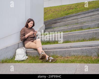 Die Frau gehäkelt draußen. Ruhige Freizeit für Frauen im städtischen Park. Anti-Stress-Hobby. Stockfoto