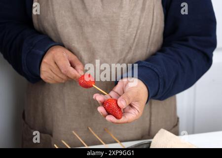 Weibliche Hand macht Obstspieße mit frischer Erdbeere, Prozess-Herstellung Tanghulu oder Frucht Satay beschichtet mit Schokolade Stockfoto