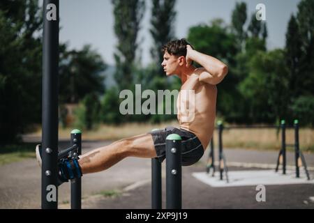 Junger Mann, der in einem Park bauchübungen auf Fitnessgeräten im Freien durchführt Stockfoto