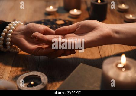 Wahrsagerin liest Zeilen auf Frauenpalme am Holztisch, Nahaufnahme. Chiromantie Stockfoto