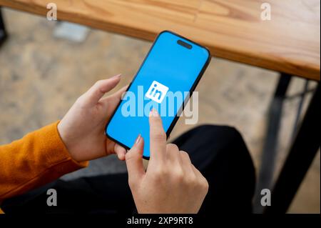 Chiang mai, Thailand - 1. August 2024: Ein Nahaufnahme einer Frau, die drinnen sitzt und die LinkedIn App auf ihrem iPhone nutzt. Das LinkedIn App-Logo auf einem s Stockfoto