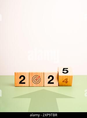 Neue Ziele neues Jahr 2025 Konzept Banner. Pfeil zum Zielsymbol mit umklappbaren Holzwürfelblöcken mit 2024 in 2025 Kalendernummern auf gre geändert Stockfoto