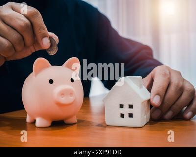 Immobilieninvestitionen, Immobiliendarlehen, Immobiliengewinn, Finanzkonzepte. Weißes Miniaturmodell auf Holztisch und Mann, Person steckte eine Münze in pi Stockfoto