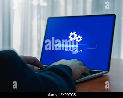 System-Update-Konzept. Zahnradsymbol und Aktualisierungssystem, Ladefortschritt der Registerkartenleiste auf blauem Bildschirm, während Geschäftsmann mit Laptop-Computer arbeiten Stockfoto