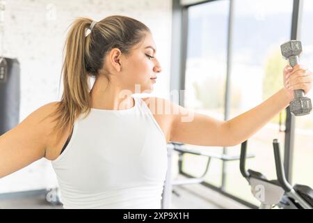 Junge lateinfrau, die auf ihren Arm schaut, während sie eine Hantel während des Trainings in einem Fitnessstudio hebt Stockfoto