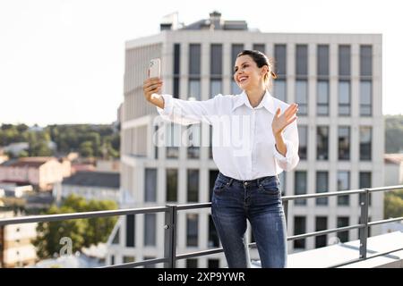 Frau, die Selfie auf dem Dach macht, Hand winkt und lächelt Stockfoto