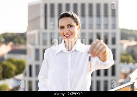 Frau mit Hausschlüsseln, die auf dem Dach der Stadt lächelt Stockfoto