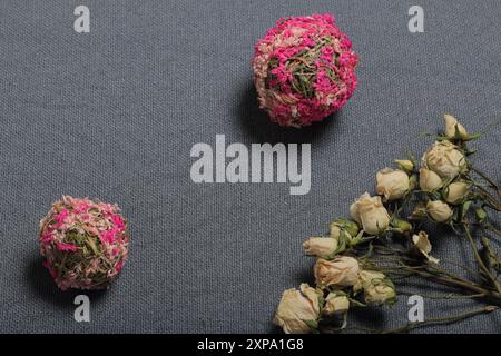 Getrocknete beige Rosen. Vor dem Hintergrund der grauen Textur des Gewebes. In der Nähe befinden sich zwei dekorative Kugeln aus getrocknetem Gras in verschiedenen Farben. Stockfoto