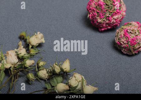 Getrocknete beige Rosen. Vor dem Hintergrund der grauen Textur des Gewebes. In der Nähe befinden sich zwei dekorative Kugeln aus getrocknetem Gras in verschiedenen Farben. Stockfoto