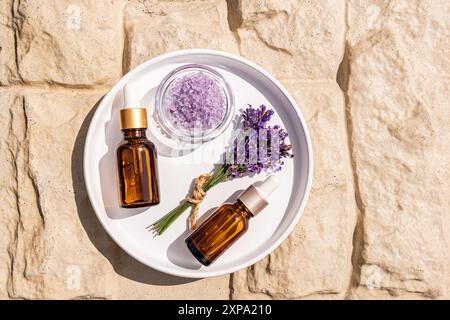 Zwei Kosmetiktropfflaschen mit einem Naturprodukt zur Selbstpflege auf Basis von Lavendelöl auf einer weißen Schale mit einem Lavendelstrauß. Spa-Anwendungen. Stockfoto