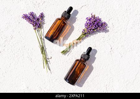 Zwei kosmetische Tropfflaschen mit einem natürlichen Heilmittel, Öl, Serum für Gesichts- und Körperhautpflege auf weißem Hintergrund zwischen Lavendelzweigen. Draufsicht Stockfoto