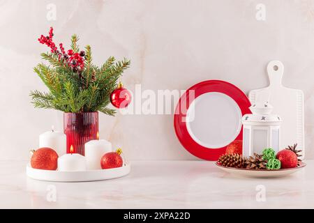 Festliche Weihnachtsdekoration auf der Küchenarbeitsplatte in traditionellen rot-weißen Farben. Ein Blumenstrauß aus Fichtenzweigen mit Kugeln, eine Laterne Stockfoto