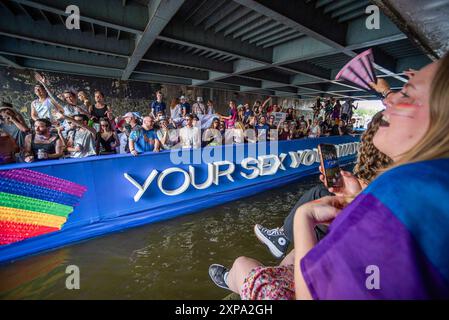 Wohlwollende jubeln vorbeifahrende Boote unter einer Brücke an, während der GEMEINSAM - Chanal Boat Pride. Der Amsterdamer „Chanal Boat Pride - Together“ ist einer der wichtigsten Höhepunkte des Amsterdamer Kalenders und kann rund 500.000 Menschen anziehen. Dies war die 27. Ausgabe. In diesem Jahr gab es 80 Boote, die am Mittag starteten und fünf bis sechs Stunden später ausliefen. Bei idealen Wetterbedingungen segelten sie vom Oosterdok über Nieuwe Herengracht, Amstel und Prinsengracht bis zum Westerdok. Viele Häuser waren in „Pride“-Farben dekoriert, mit einer stimmungsvollen und festlichen Atmosphäre entlang des Weges. Stockfoto