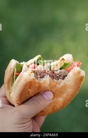 Hand hält hausgemachten gegrillten Hamburger mit großem Biss. Im Sommer Grill im Freien. Stockfoto