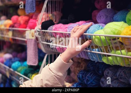 Die Hand greift nach bunten Garnbällen in einem Ladenregal. Nahaufnahmen für Design und Druck. Stockfoto