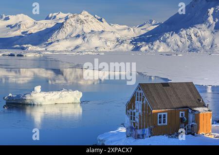 Typisches grönländisches Haus vor Eisbergen und Bergen, Winter, sonnig, Kulusuk, Ostgrönland, Grönland Stockfoto