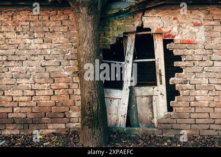 Altes, ruiniertes Haus mit beschädigter Ziegelmauer und kaputten Türen, bereit für die Vernichtung Stockfoto