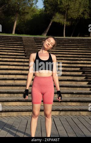 Eine junge Frau mit rotem Haar führt im Rahmen ihrer Pilates-Routine in einer natürlichen Umgebung im Freien Kopfdrehungen durch und betont dabei körperliche und Männer Stockfoto