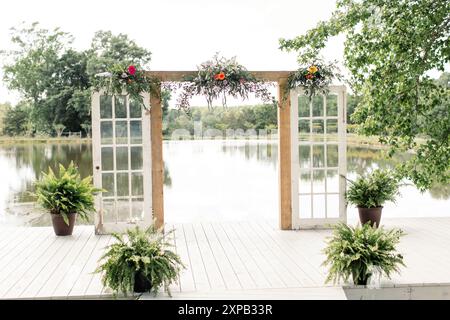 Hochzeitsbogen mit Blumen und Grün auf einer Plattform am See. Stockfoto
