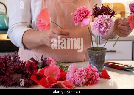 Frau, die einen Blumenstrauß in einer Vase auf einer Arbeitsplatte arrangiert Stockfoto